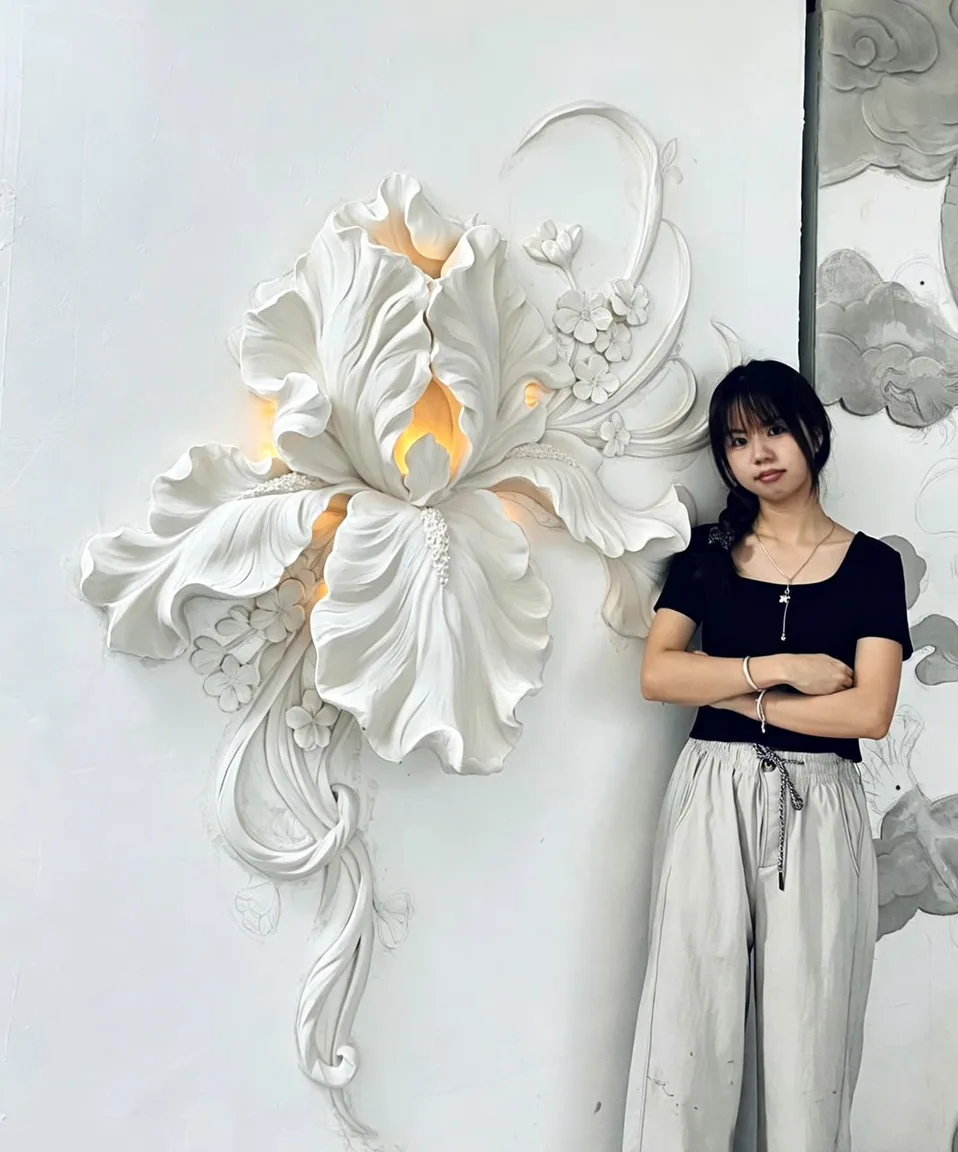 Person with crossed arms beside an illuminated white floral wall relief